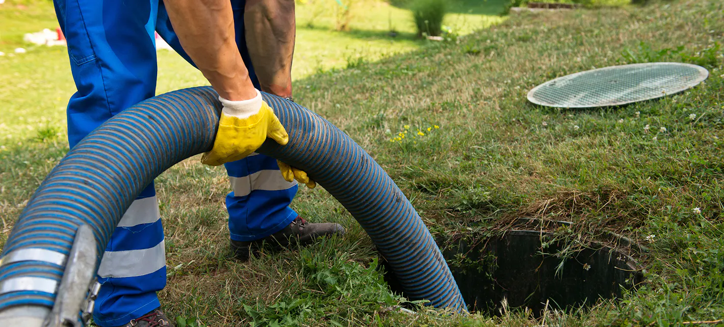 Slam pumpes opp fra et slamanlegg, en person holder slangen som går ned i anlegget