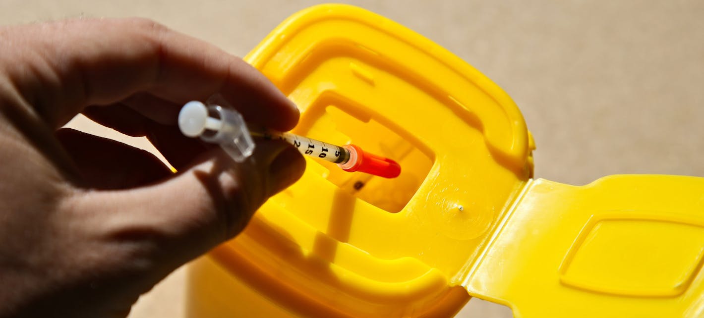 Bilde av en brukt sprøyte som kastes i en gul beholder for medisinsk avfall