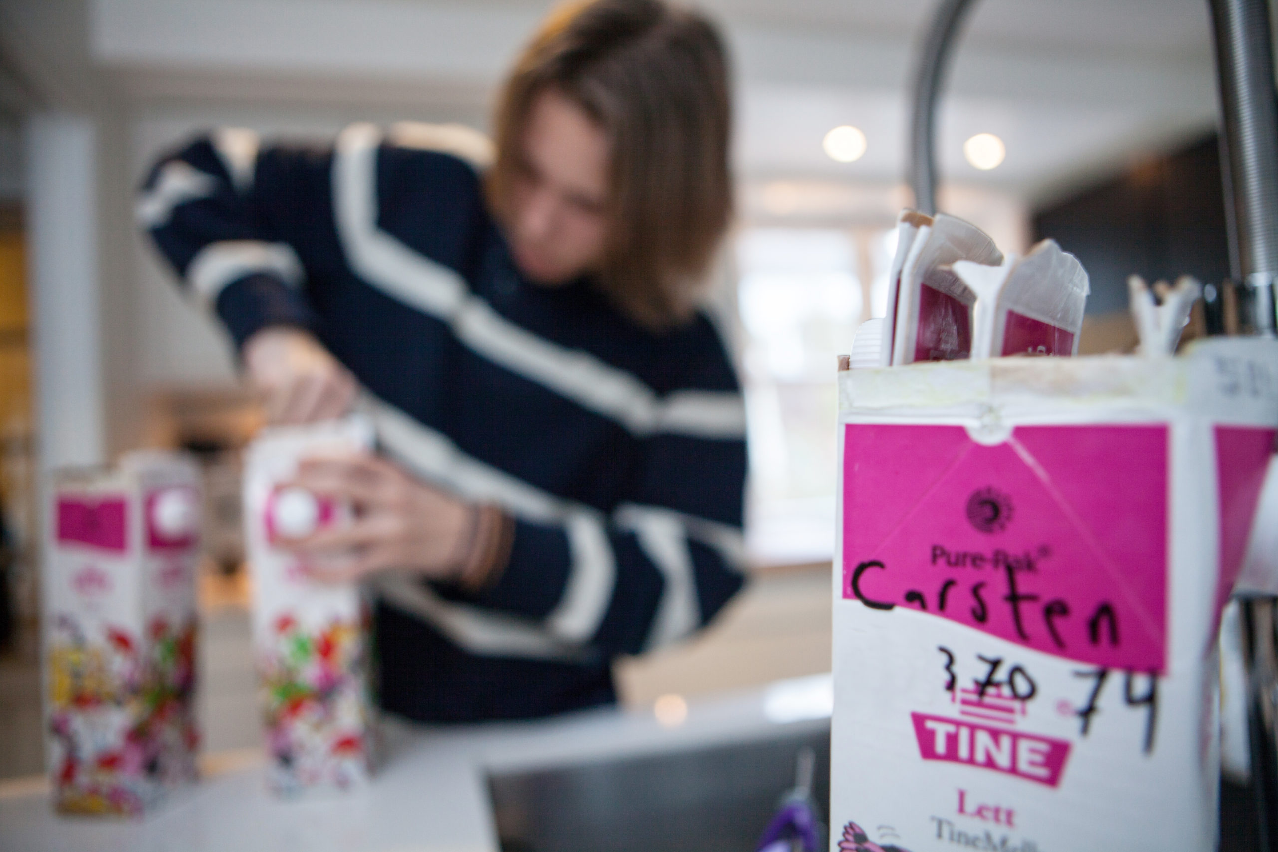 Bilde av en person på et kjøkken, som presser sammen drikkerkartonger og legger de inn i en annen drikkekartong