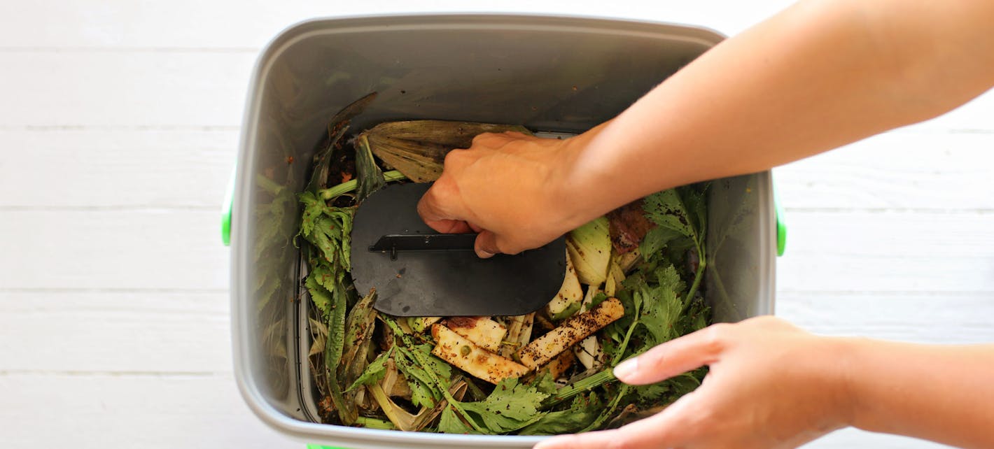 Detalj av to armer som strekker seg ned i en bokashibøtte for å presse sammen matavfallet