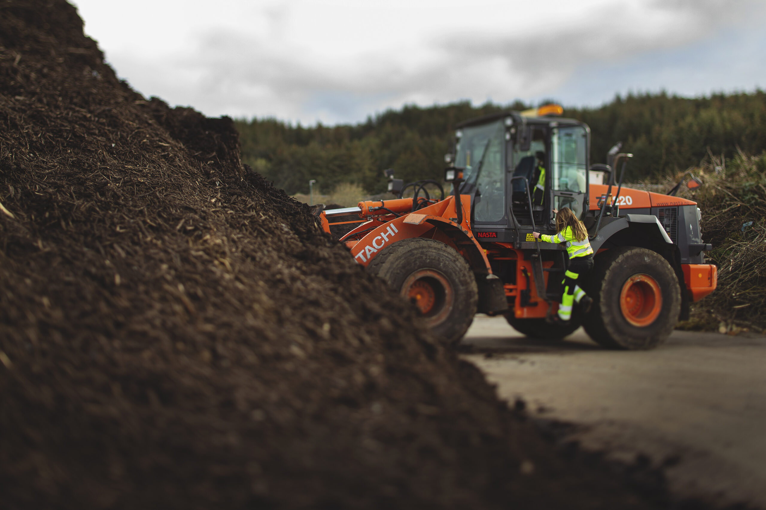 Traktor inne på området med kompost på Årabrot miljøpark. En HIM-ansatt er på vei opp i traktoren.