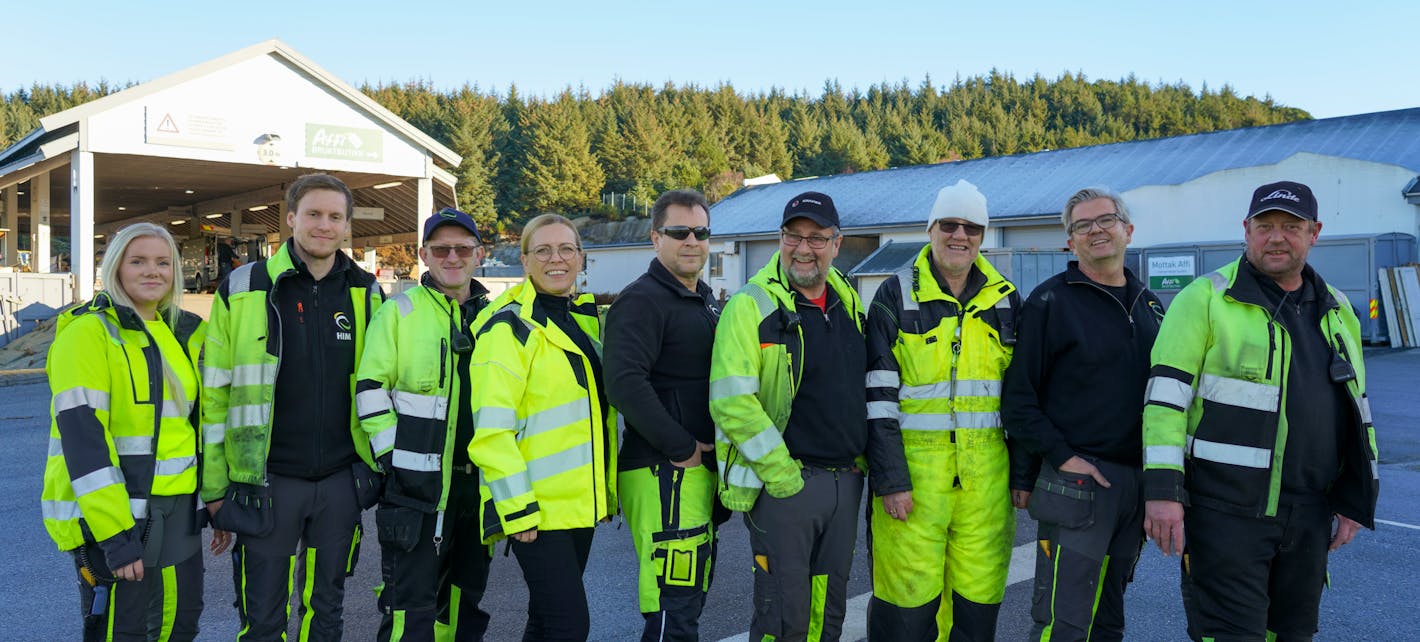En gjeng HIM-medarbeidere fra drift på Årabrot inne på miljøparken. De står side om side foran rampen, i gule arbeidsklær.