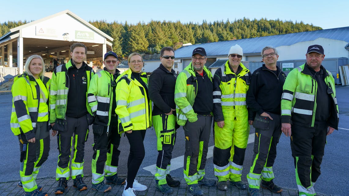En gjeng HIM-medarbeidere fra drift på Årabrot inne på miljøparken. De står side om side foran rampen, i gule arbeidsklær.