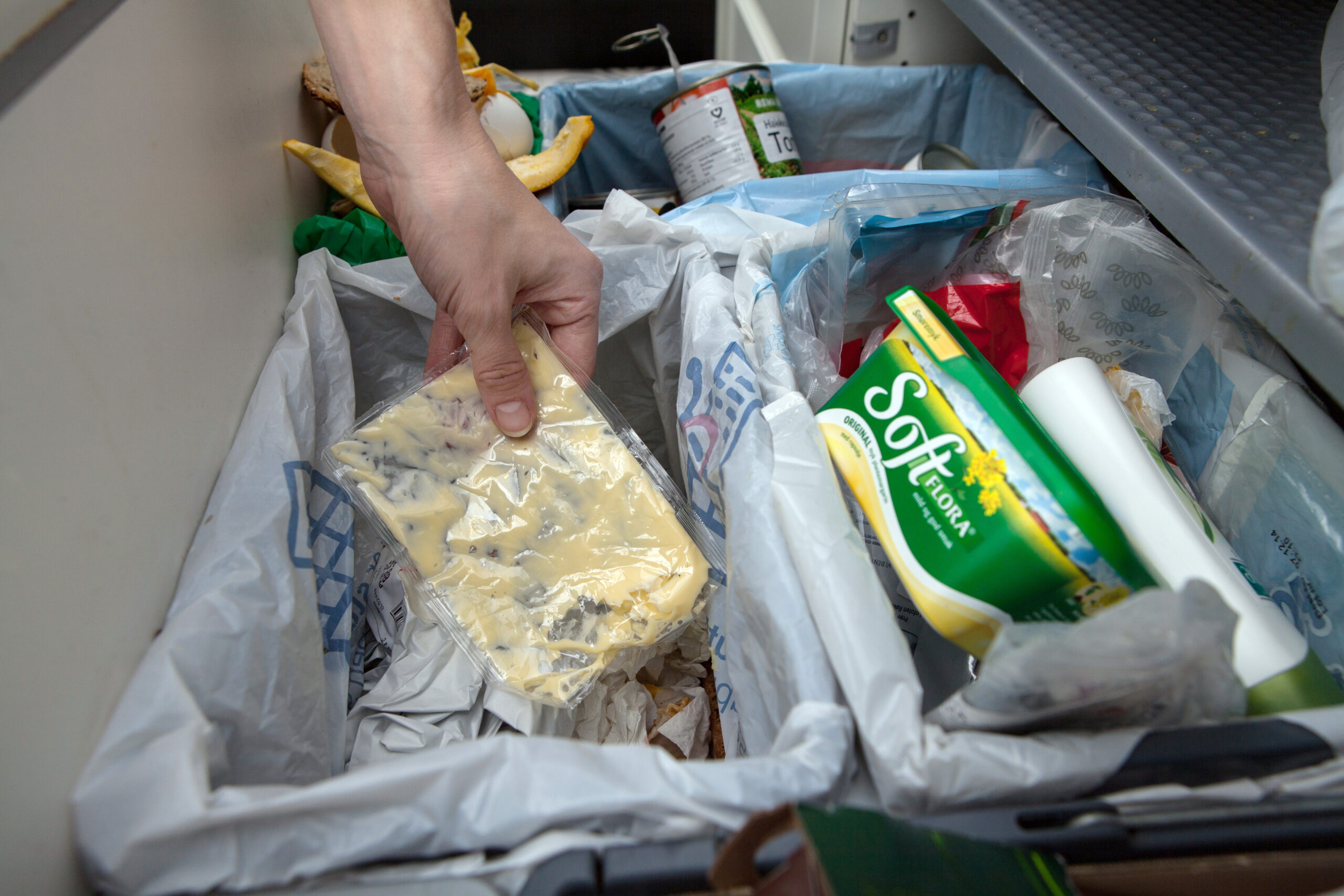 Flere avfallsbeholdere i en kjøkkenskuff, der en person kaster en pose med majonesrester