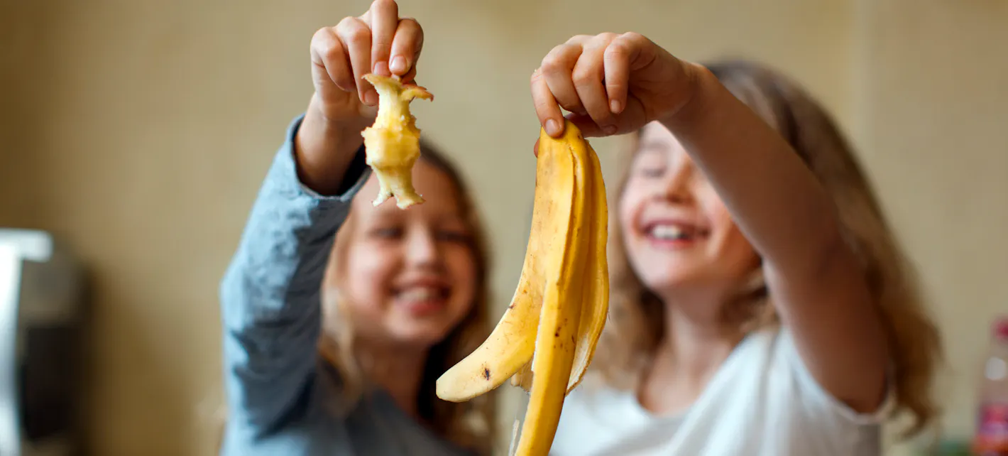 To jenter holder frem en epleskrott og et bananskall