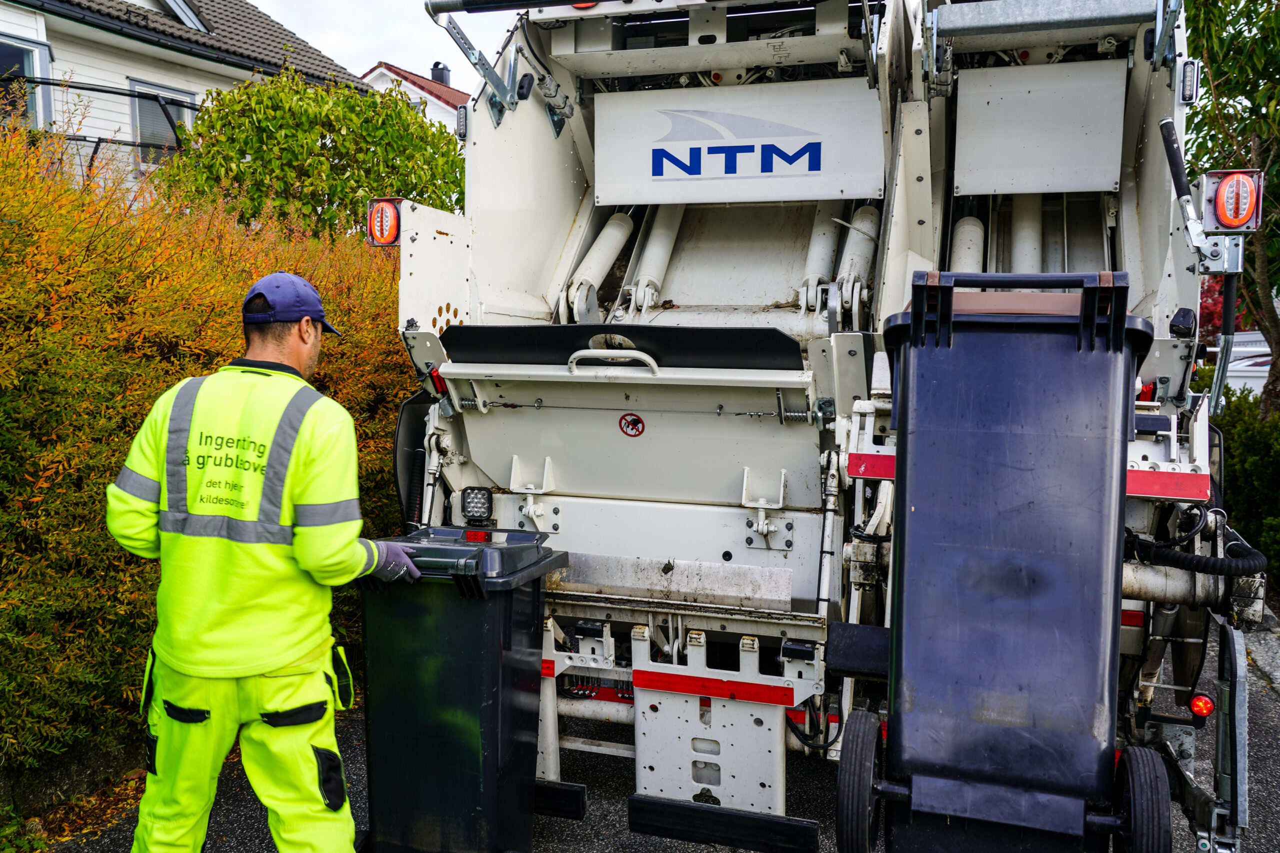 Renovatør står med ryggen til og tømmer en avfallsdunk i renovasjonsbilen